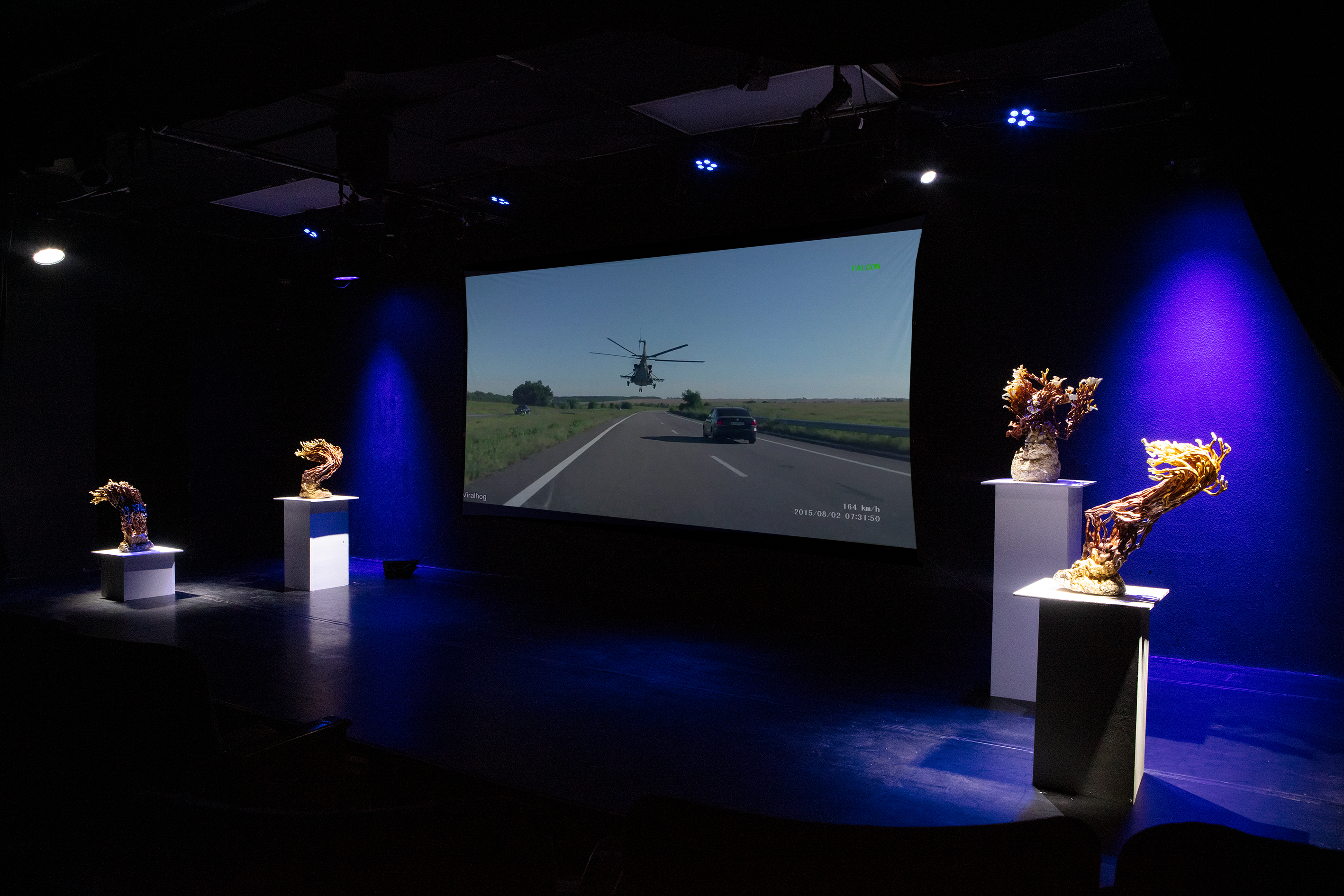 3/4 right installaion view of a projecion screen in a dark theater with two sculptures on both the left and right sides of the screen illumated by spotlights